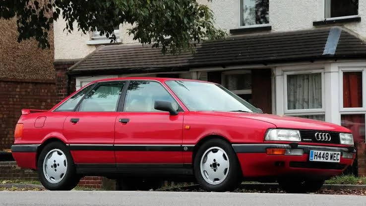 Punane auto, audi 90, hõbedastel velgedel värava ees parkimas